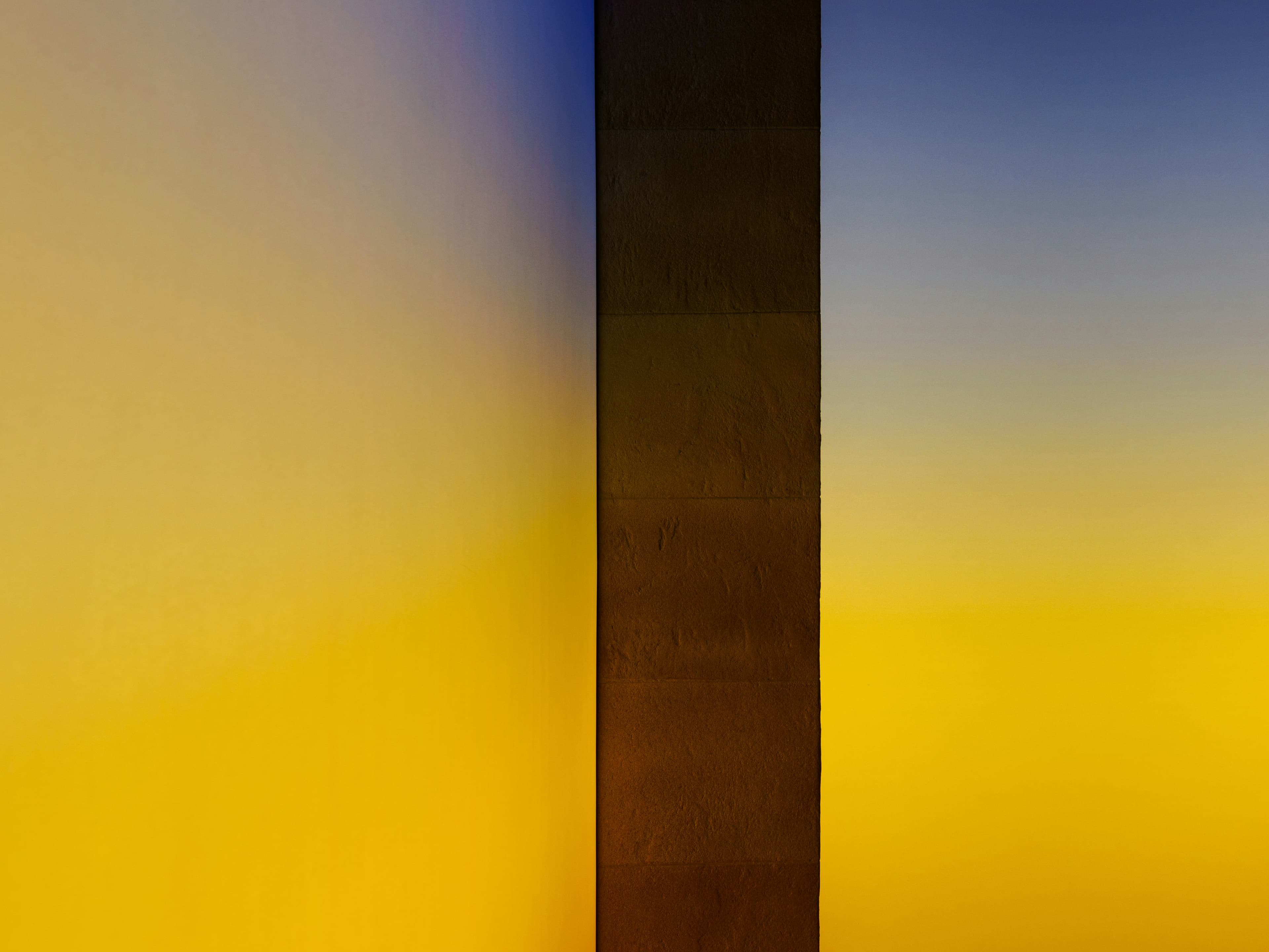 An architectural column dividing illuminated fields of yellow and blue